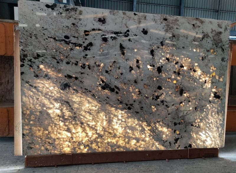 White granite slab with dark veining and black mineral clusters, partially backlit to reveal its natural translucency